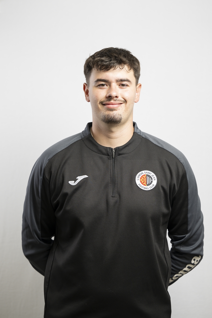 Portrait de Hugo Lennon, &eacute;ducateur de l&rsquo;Union Saint-Jean Football Club, v&ecirc;tu d&rsquo;un surv&ecirc;tement noir avec le logo du club.