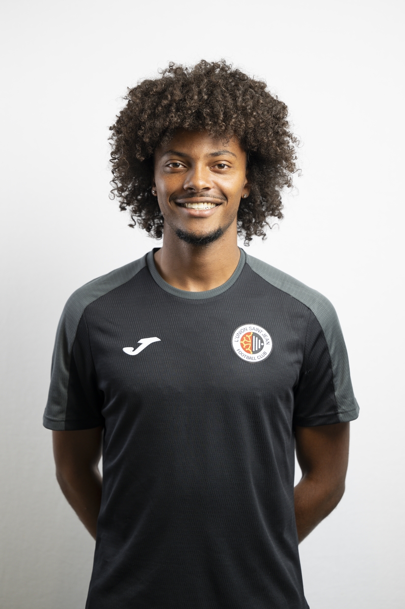 Portrait de Lillian Gallas, membre du staff de L&rsquo;Union Saint-Jean Football Club, souriant, v&ecirc;tu d&rsquo;un t-shirt noir Joma avec le logo du club, sur fond clair.