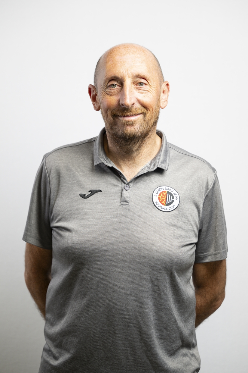 Portrait de St&eacute;phane Aused, &eacute;ducateur de l&rsquo;Union Saint-Jean Football Club, en tenue officielle grise avec le logo du club.