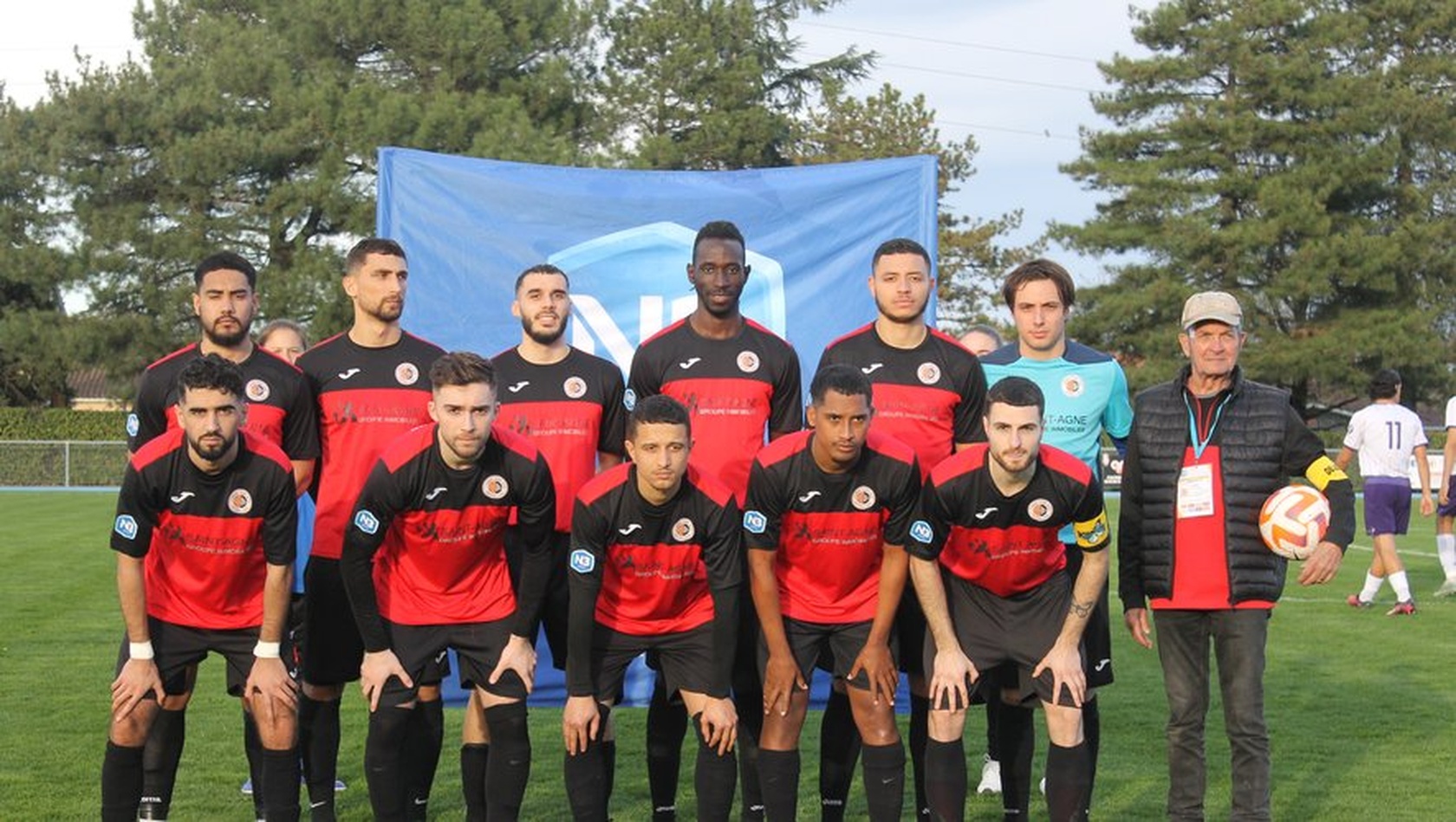 &Eacute;quipe de football en tenue rouge et noire posant devant une banderole 