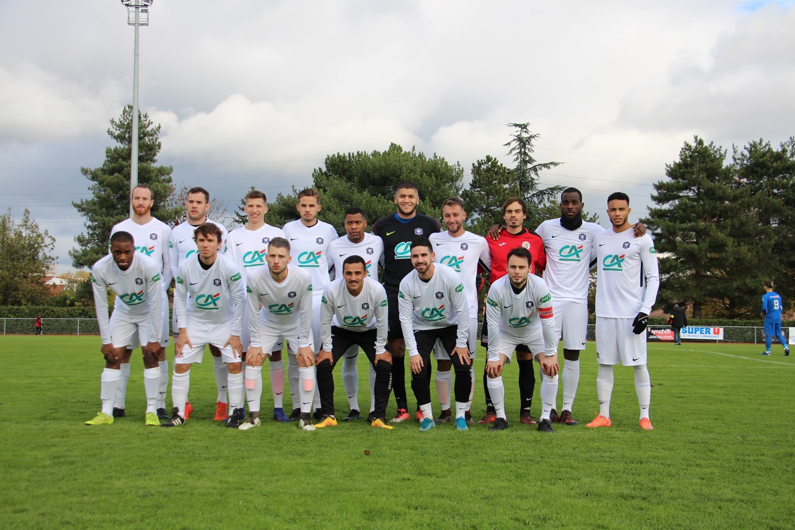 Photo d&rsquo;&eacute;quipe de football posant en deux rang&eacute;es sur le terrain avant un match de Coupe de France, joueurs en maillot blanc avec logo du Cr&eacute;dit Agricole.