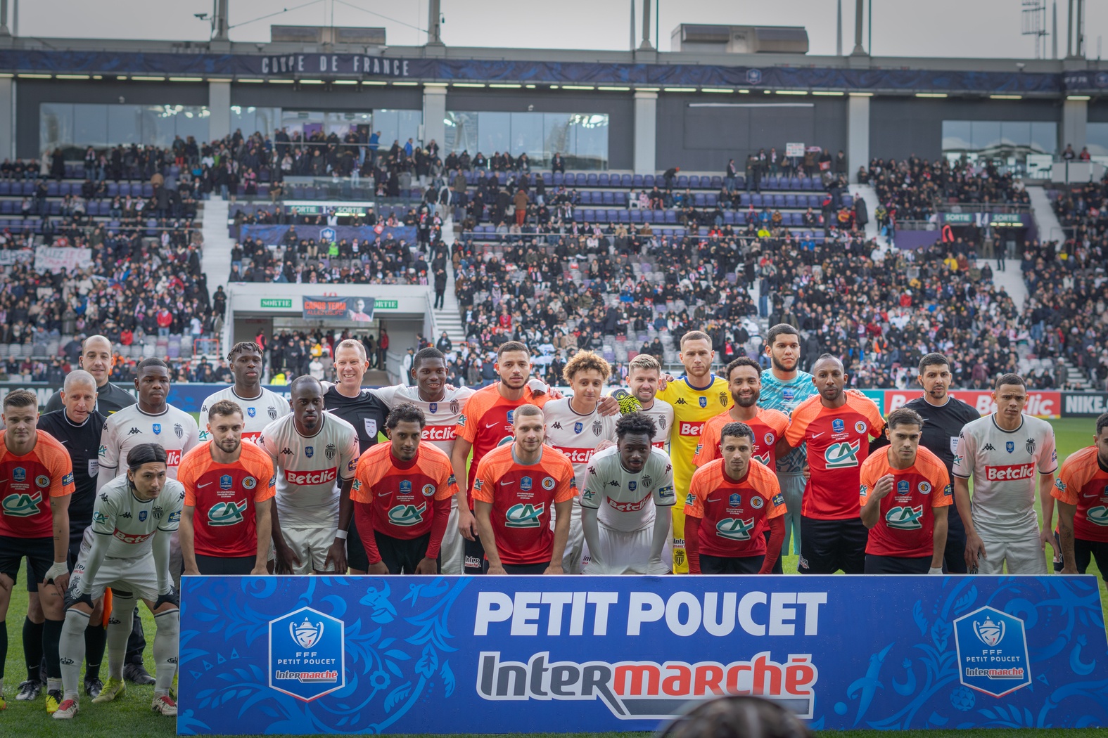 Photo officielle des joueurs de l&rsquo;Union Saint-Jean et de l&rsquo;AS Monaco avant un match de Coupe de France, posant ensemble derri&egrave;re une banderole 