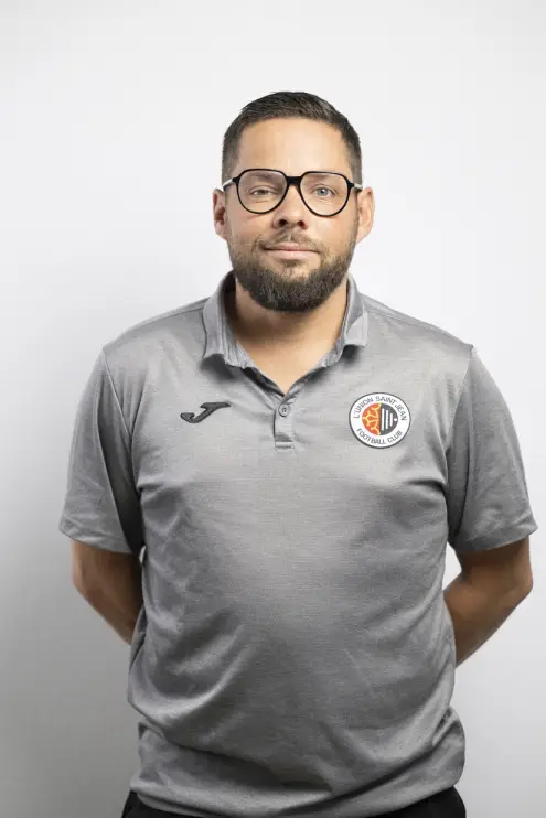 Portrait d’Anthony Bazin, membre du staff de L’Union Saint-Jean Football Club, en polo gris Joma avec le logo du club, sur fond clair.