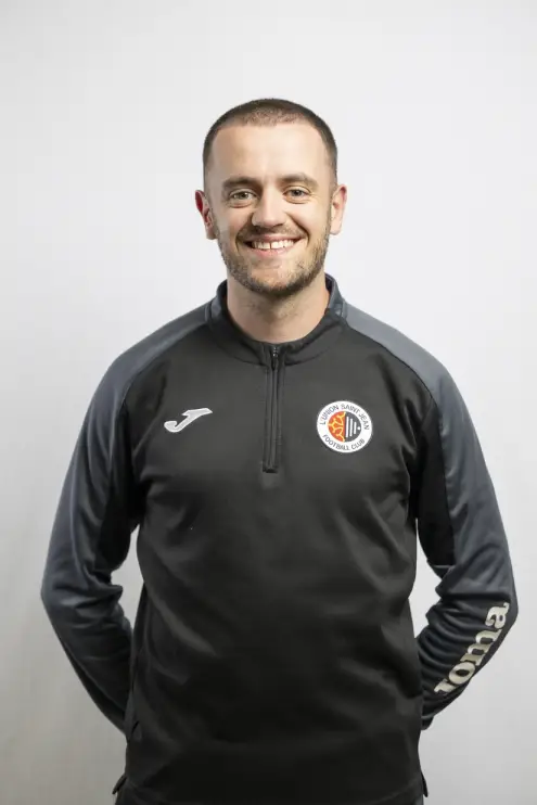 Portrait de Valentin Gayraud, membre du staff de L’Union Saint-Jean Football Club, en tenue noire Joma avec le logo du club, sur fond clair.