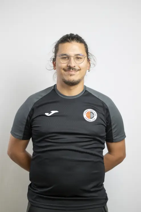 Portrait de Ryad Daho, membre du staff de L’Union Saint-Jean Football Club, en tenue noire Joma avec le logo du club, sur fond clair.