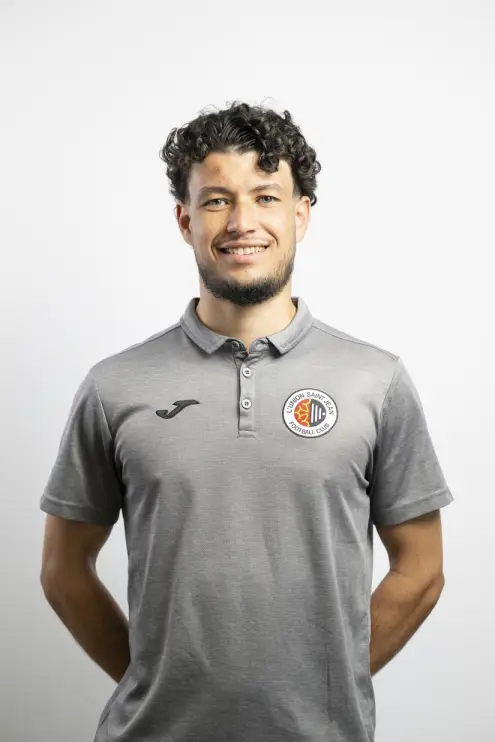 Portrait de Rayan Benarioumlil, membre du staff de L’Union Saint-Jean Football Club, en polo gris Joma avec le logo du club, sur fond clair.