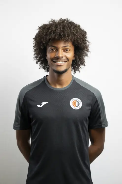 Portrait de Lillian Gallas, membre du staff de L’Union Saint-Jean Football Club, souriant, vêtu d’un t-shirt noir Joma avec le logo du club, sur fond clair.